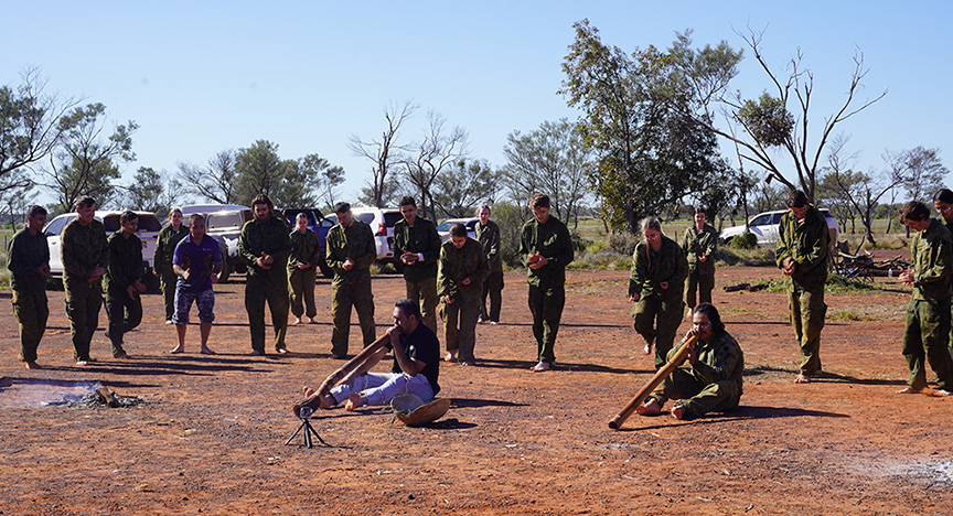 Two Aboriginal men playing didgeridoo and a group of young people dancing around them.