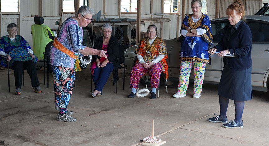 An elderly woman playing a game during Charleville Seniors Games and group of women watching her play.