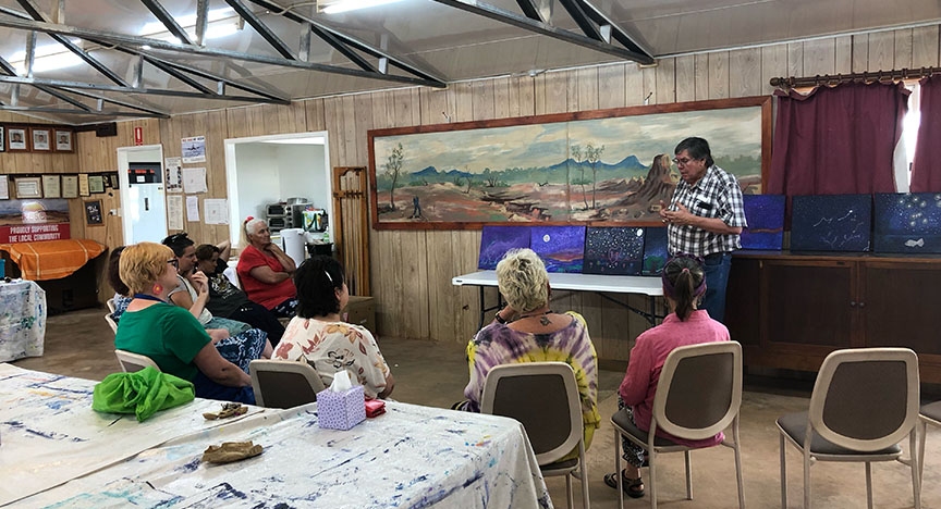 A group of people sitting down in semi circle listening to a man during art and wellbeing workshop.