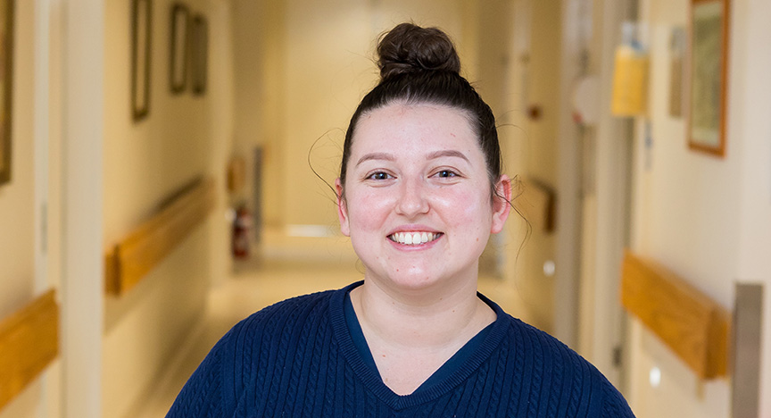 A woman wearing a navy jumper standing in a hospital corridor.